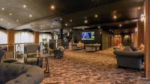 A hotel lobby with seating areas, a television screen, and a staircase. - Otter Lodge (Chorley)