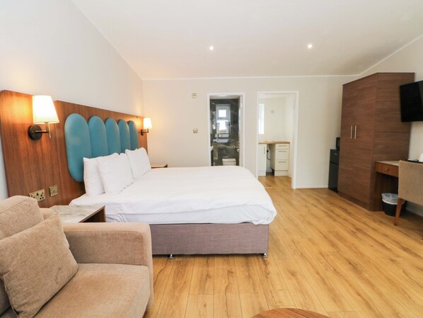 Una camera d'albergo moderna con un letto grande, una testiera in legno, una zona salotto con un divano, un armadio in legno e una televisione.