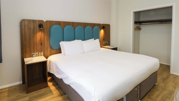 Une chambre d’hôtel avec un grand lit, une tête de lit en bois, des tables de chevet et une armoire.