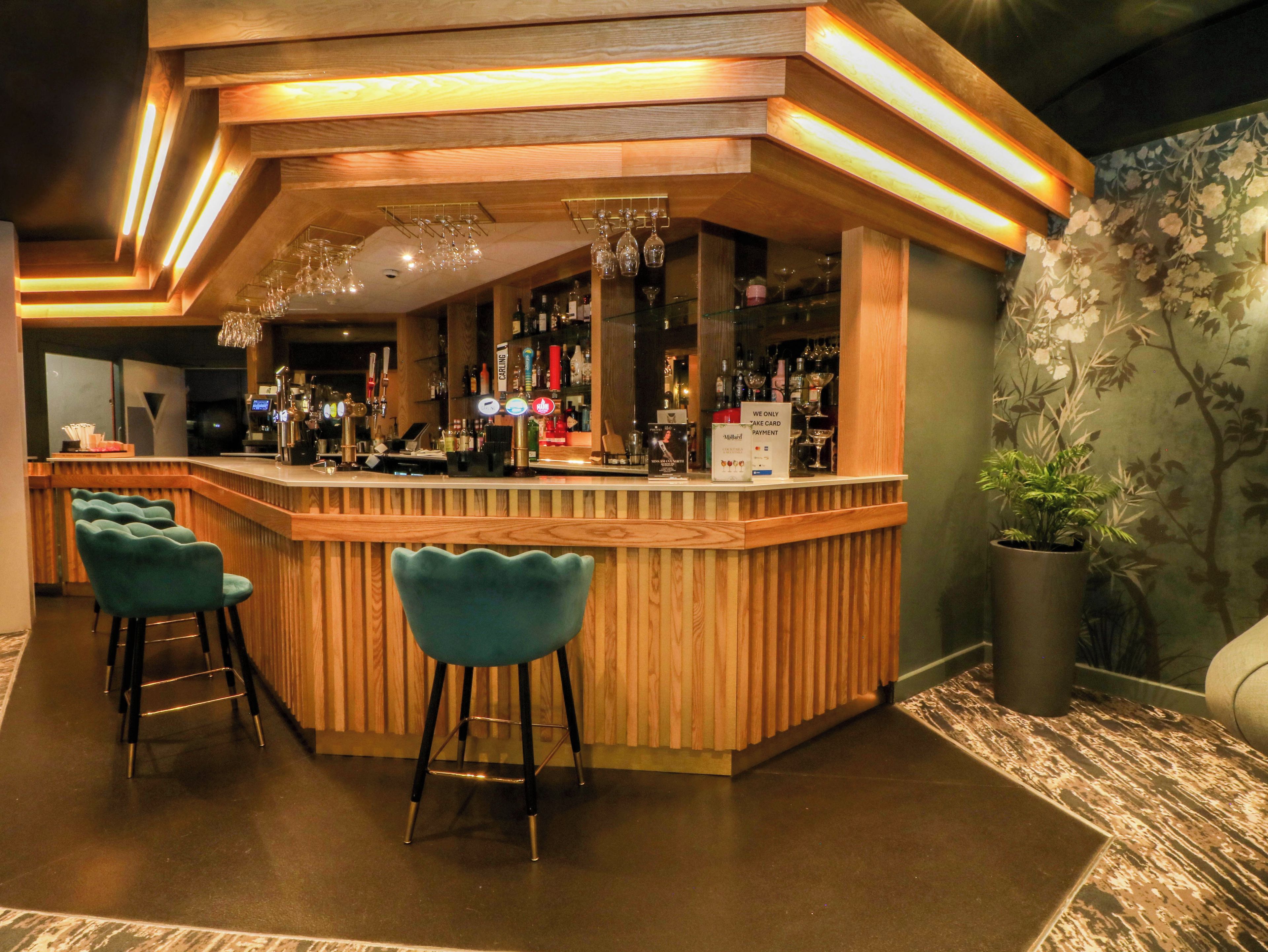 A bar area with wooden bar counter, bar stools, and a potted plant.