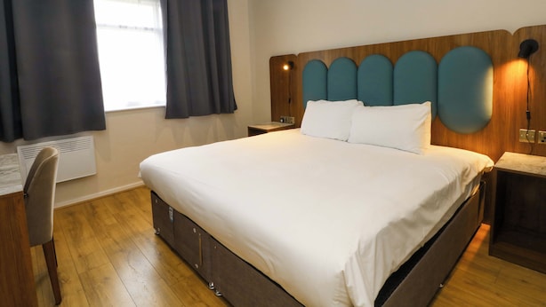 Ein Hotelzimmer mit einem großen Bett, einem Schreibtisch und einem Fenster mit Vorhängen.