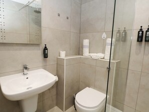 Une salle de bain équipée d’un lavabo, de toilettes, d’une douche et d’étagères où sont rangés les articles de toilette.