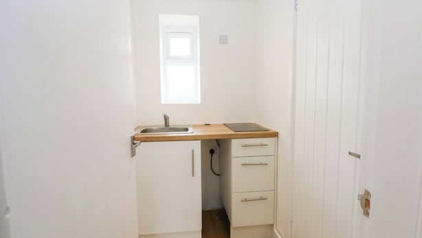 Een compacte kitchenette met een spoelbak, een houten aanrechtblad en twee lades.