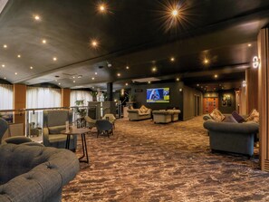 A hotel lobby with seating areas, a television screen, and a staircase. - Badger Lodge (Chorley)