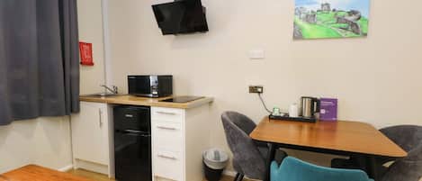 A compact kitchenette with a microwave, oven, and sink, a dining table with chairs, and a painting on the wall.