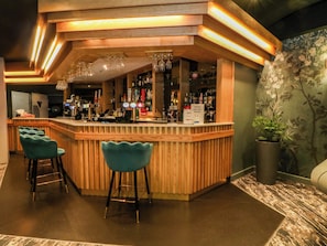 Zona de bar con mostrador de madera, taburetes y una planta en maceta.
