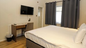 A bedroom with a bed, a desk, a chair, a TV, and a window with curtains. - Owl Lodge (Chorley)