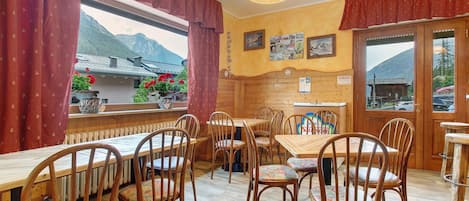 A restaurant with wooden tables and chairs, a view of mountains through large windows, and a wooden interior.