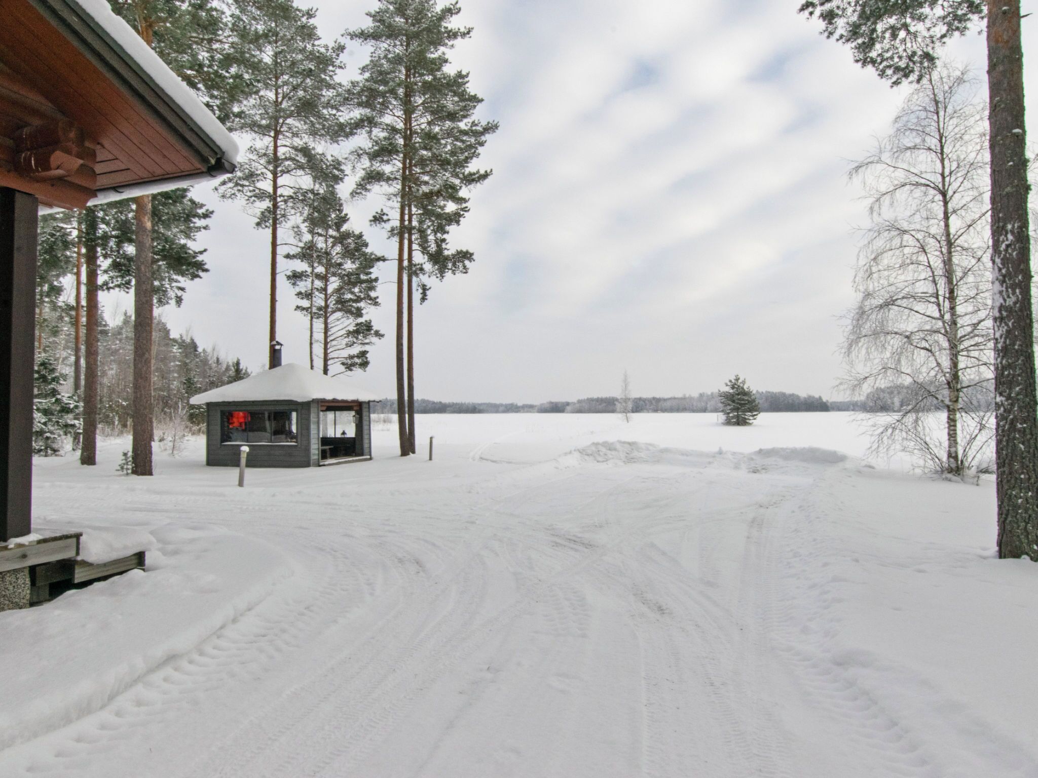 A cabin with a snow-covered roof, surrounded by tall trees and a snowy landscape.