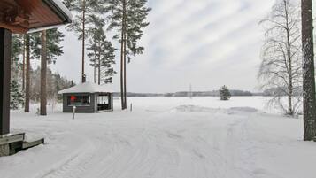 A cabin with a snow-covered roof, surrounded by tall trees and a snowy landscape.