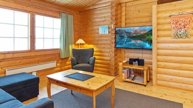 Et værelse i en træhytte med træpaneler, et fjernsyn, et bord, en sofa og en lampe.