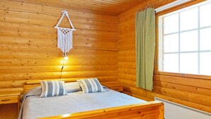 Et hyggeligt værelse i en træhytte med seng, ophængt makramépynt, et vindue med gardiner og en radiator.