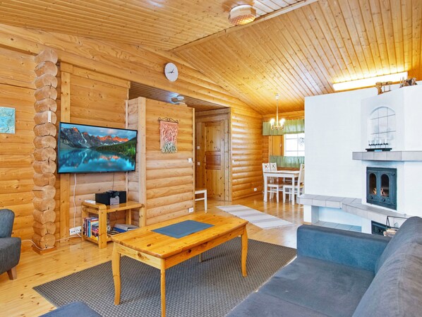 Ein rustikales Holzhaus-Interieur mit Fernseher, Holzmöbeln, Kamin und Essbereich.