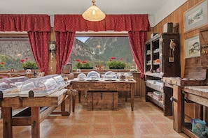 A rustic dining area with a wooden table, red curtains, and a mountain view. - "Room 9" with Mountain View, Shared Terrace in Bionaz (Dzovennoz)