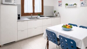 Eine moderne Küche mit weißen Schränken, einer Mikrowelle, einem Spülbecken und einem Essbereich mit Tisch und blauen Stühlen.