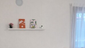 Ein Wohnzimmer mit einem beigen Sofa, gestreiften Kissen, einem Teppich mit roten und schwarzen Mustern, einem weißen Couchtisch und einem weißen Regal mit Dekoration.