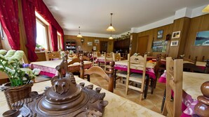 Um restaurante com paredes de madeira, várias mesas com cadeiras, luminárias pendentes e uma grande peça decorativa sobre a mesa.