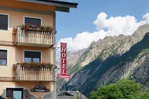 A hotel with a mountain backdrop, featuring a signboard with the hotel's name and a welcoming entrance. - "Room 10" with Mountain View, Shared Terrace in Bionaz (Dzovennoz)