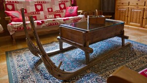 Uma cadeira de balanço de madeira tradicional com mesa de vidro, um tapete estampado e um sofá com almofadas de corações.