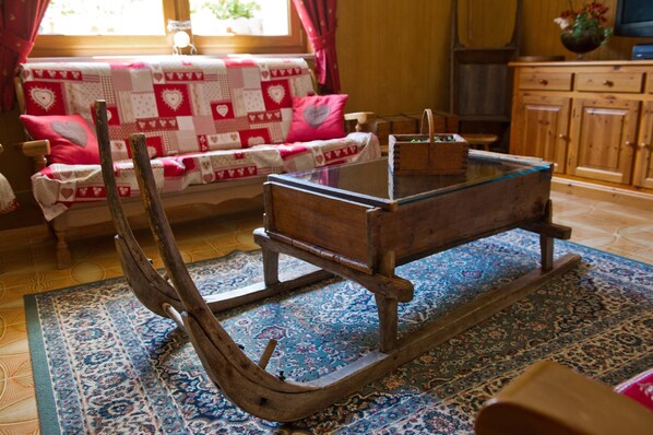A traditional wooden rocking chair with a glass top, a patterned rug, and a sofa with heart-patterned cushions. - "Room 10" with Mountain View, Shared Terrace in Bionaz (Dzovennoz)