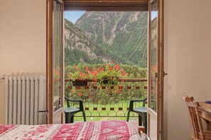 A balcony with a view of a mountainous landscape, a radiator, and a bed with a patterned bedspread. - "Room 10" with Mountain View, Shared Terrace in Bionaz (Dzovennoz)