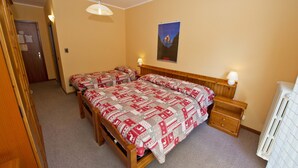 Quarto com duas camas, cabeceiras de madeira, mesas de cabeceira com luminárias, um pôster na parede e um radiador.