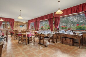 A dining area with wooden tables and chairs, a buffet setup, and a view of a mountainous landscape through large windows. - "Room 10" with Mountain View, Shared Terrace in Bionaz (Dzovennoz)