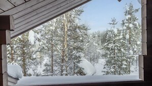 Uma floresta coberta de neve vista através de um janelão de madeira.