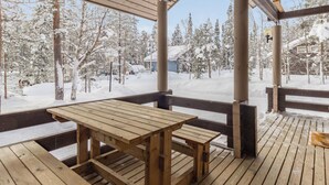 Um deck de madeira com uma mesa de piquenique e bancos, com vista para uma paisagem nevada com árvores e edifícios.
