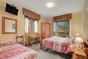A bedroom with two beds, a desk, a chair, a television, and a window with curtains. - Triple Room 11 with Mountain View and Shared Terrace in Bionaz (Dzovennoz)