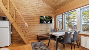 Een houten cabin met een eethoek, een aan de muur bevestigde televisie en een trap.
