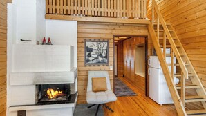 Een gezellig chaletinterieur met een open haard, een houten trap en een eethoek.
