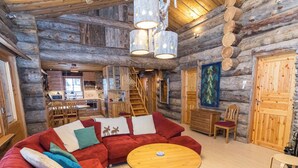 Ein Holzblockhaus-Interieur mit einem roten, modularen Sofa, einem Holzesstisch und einer Küchenzeile.