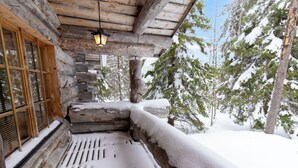 Eine Blockhütte mit einer Holzterrasse, einer Laterne und verschneitem Gelände.