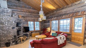 Ein Holzblockhaus-Interieur mit Kamin aus Stein, einem roten Sofa, einem Holztisch und großen Fenstern.