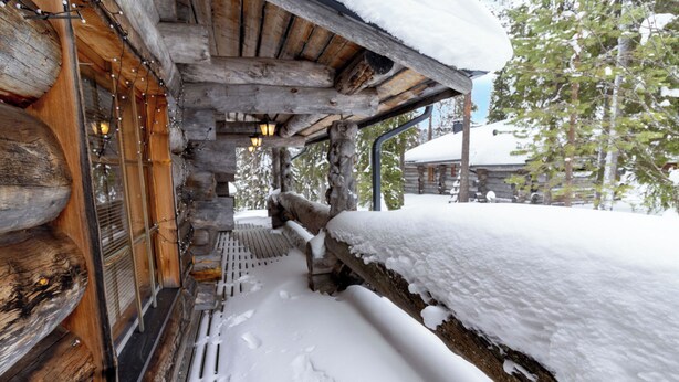 Eine Blockhütte mit verschneiter Fassade, Holzbalken und einer Holzterrasse.