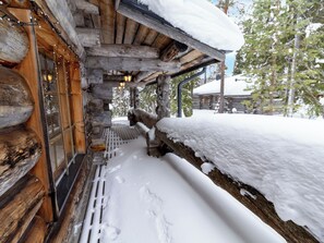 Eine Blockhütte mit verschneiter Fassade, Holzbalken und einer Holzterrasse.