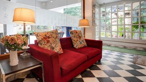 A red sofa with floral cushions, a small table with a vase of flowers, and a checkered floor. - Super Deluxe Room Hotel Mayvilas (Dehradun)