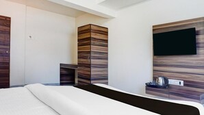 Ett modernt hotellrum med en säng, en garderob, en platt-TV som är monterad på väggen och ett litet bord med en vattenkokare.