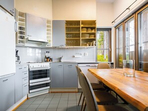 A modern kitchen with a built-in oven, a dining table, and a window with a view of greenery. - Rukatunturintie 8 g2 by Interhome (Kuusamo)