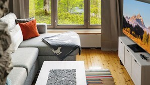 A living room with a sofa, a television, and a large window with a view of trees and mountains. - Rukatunturintie 8 g2 by Interhome (Kuusamo)