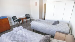 Une chambre avec deux lits, un bureau avec un ordinateur portable, deux chaises et une armoire.