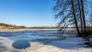 Un lac gelé, le sol recouvert de neige et des arbres sans feuilles.