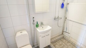 Une petite salle de bain propre, avec des carreaux blancs, un lavabo blanc, des toilettes et une douche.