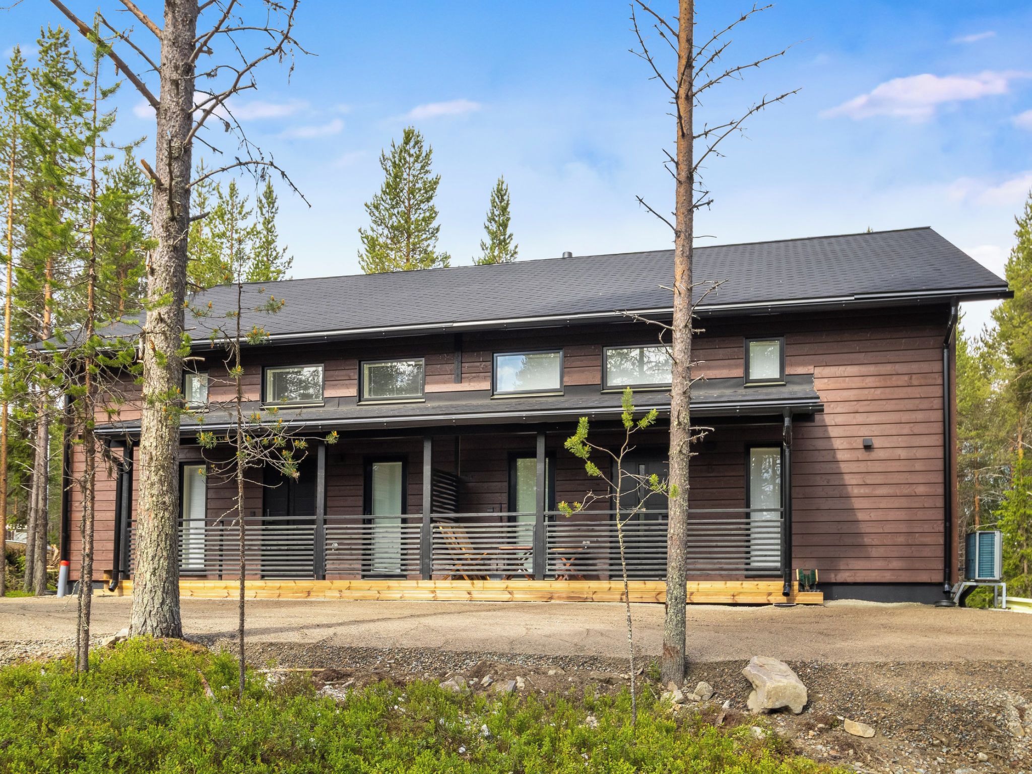 Kaksikerroksinen talo, jonka ulkoseinät ovat tummanruskeat, siinä on katettu kuisti ja sorapäällysteinen ajotie.