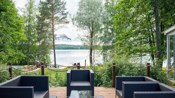 Una terraza con muebles de mimbre dando a un lago, rodeada de árboles.