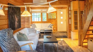 Interior de una cabaña de troncos con un sofá, un sillón y una mesa de comedor.