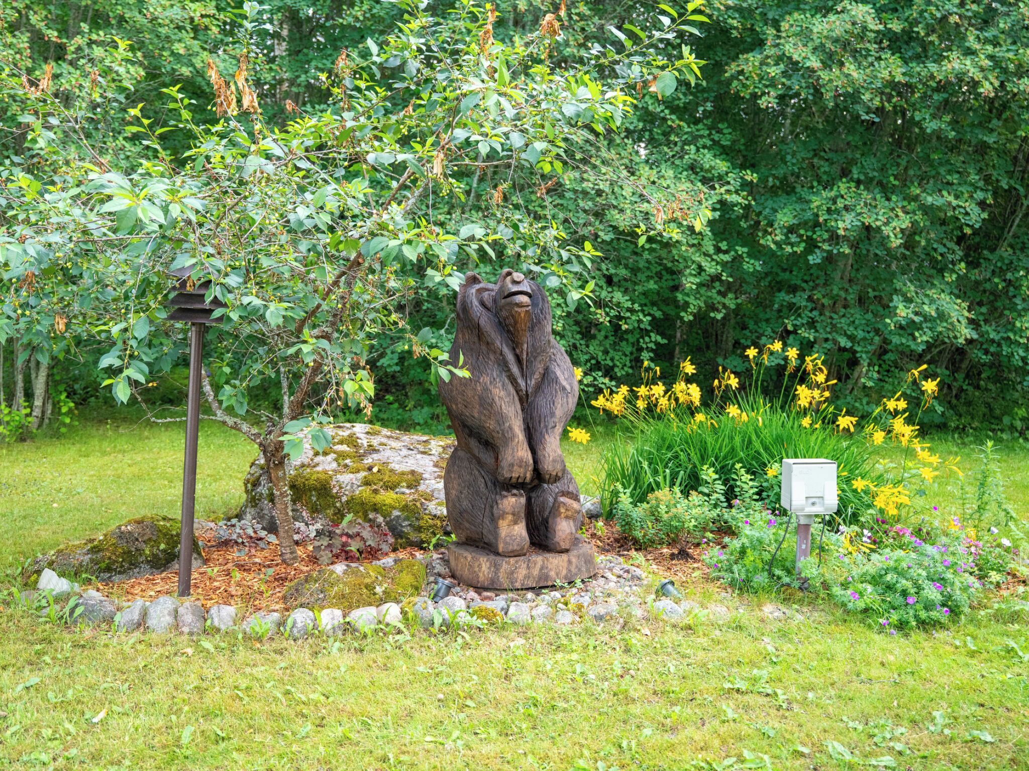 Una estatua de jardín de un oso, rodeada de follaje y flores.