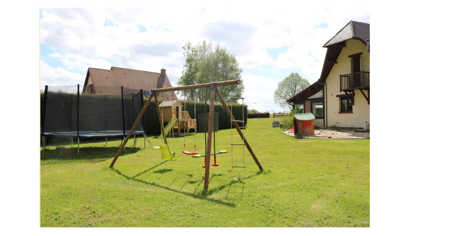 A grassy outdoor area with a swing set, a trampoline, and a small playhouse.