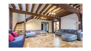 Ein geräumiges Wohnzimmer mit hohen Decken, freiliegenden Holzbalken, einem blauen Sofa, einem grauen Sofa und einem Fliesenboden.